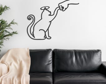 Könnte beinhalten: Schwarze Wandkunst aus Metall, die eine Katze mit Heiligenschein darstellt, die nach einer Faust greift. Die Katze und die Hand sind in Schwarz vor einem weißen Hintergrund umrissen.