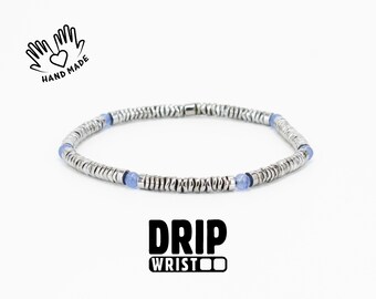 May include: A silver bracelet with small, round, textured metal beads and interspersed blue beads. The bracelet is handmade, as indicated by the text and graphic. The word "DRIP" is printed in bold, black letters, with the word "WRIST" below it.