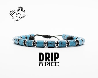 Può includere: Un braccialetto con perline blu e nere, con un cordoncino nero e un accento in metallo argentato. Il braccialetto ha la scritta "DRIP WRISTOO" stampata sotto.