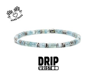 May include: A beaded bracelet with light blue and silver accents. The bracelet is made of small, square-shaped beads and silver-colored metal spacers. The words "HAND MADE" and a heart symbol are in the upper left corner. The words "DRIP WRIST" are at the bottom.