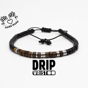 May include: A black and brown beaded bracelet with silver accents. The bracelet has a black cord with a knot closure. The text "DRIP WRISTOO" is printed below the bracelet.