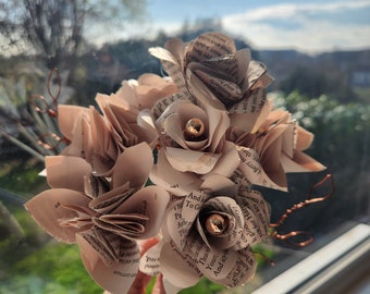 May include: A bouquet of paper flowers made from old book pages. The flowers are a light brown color and have a vintage aesthetic. The flowers are held together with copper wire.