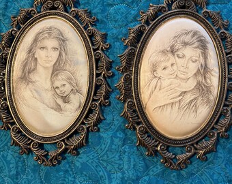 May include: Two vintage oval framed portraits. Each features a pencil sketch of a mother and child. The frames are ornate, with a bronze finish. The background is a teal blue quilted fabric.
