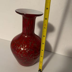 May include: A red glass vase with gold flecks. The vase has a wide base and a narrow neck. It is approximately 7 inches tall.