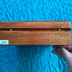 K&ouml;nnte beinhalten: Eine rechteckige Holzkiste mit dunkelbraunem Finish und Messingbeschl&auml;gen. Die Kiste hat eine glatte, polierte Oberfl&auml;che. Der Text "MICROPHONES MADE IN MEXICO" ist auf einem Etikett zu sehen. Die Kiste ist wahrscheinlich zur Aufbewahrung von Mikrofonen bestimmt.