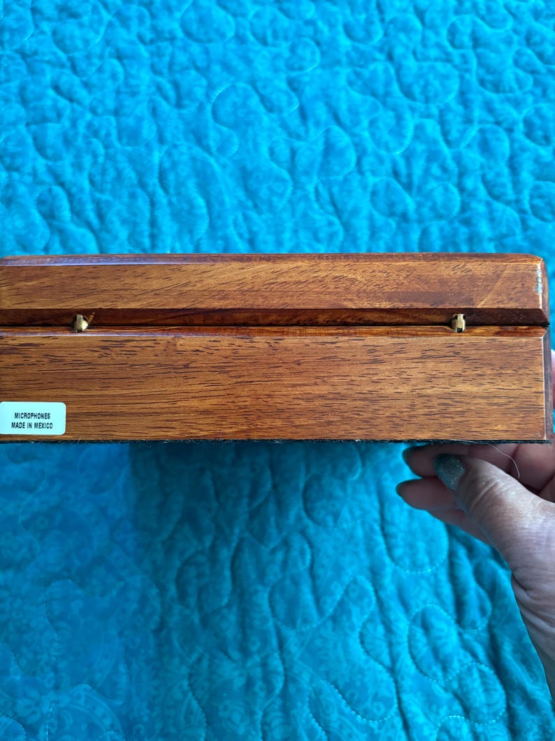 K&ouml;nnte beinhalten: Eine rechteckige Holzkiste mit dunkelbraunem Finish und Messingbeschl&auml;gen. Die Kiste hat eine glatte, polierte Oberfl&auml;che. Der Text "MICROPHONES MADE IN MEXICO" ist auf einem Etikett zu sehen. Die Kiste ist wahrscheinlich zur Aufbewahrung von Mikrofonen bestimmt.