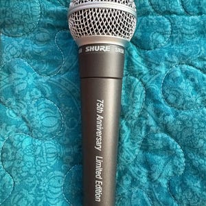 K&ouml;nnte beinhalten: Ein Shure SM58 Mikrofon mit silbernem Mesh-Kopf und dunkelgrauem Geh&auml;use. Auf dem Mikrofon steht "75th Anniversary Limited Edition". Der Hintergrund ist ein t&uuml;rkisfarbener Steppstoff.