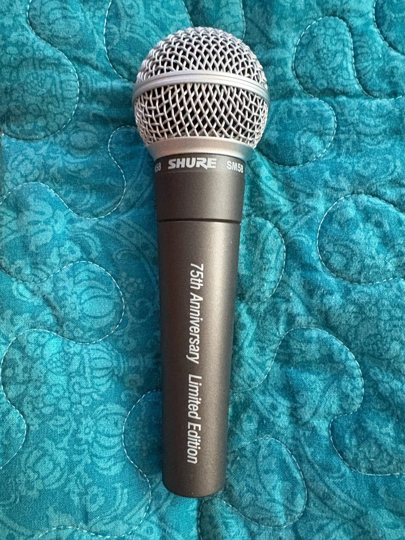 K&ouml;nnte beinhalten: Ein Shure SM58 Mikrofon mit silbernem Mesh-Kopf und dunkelgrauem Geh&auml;use. Auf dem Mikrofon steht "75th Anniversary Limited Edition". Der Hintergrund ist ein t&uuml;rkisfarbener Steppstoff.