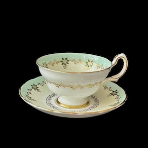 Taza de té vintage de porcelana Grosvenor China, Inglaterra, en tonos crema, blanco y azul pálido, con motivos dorados y detalles de esmalte verde.