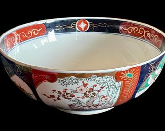 May include: A large, white ceramic bowl with a blue, red, and gold floral design. The bowl has a wide rim and a rounded bottom.