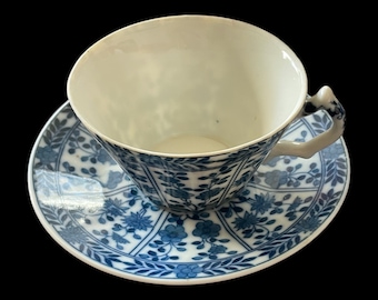 May include: A white teacup and saucer with a blue and white floral pattern. The cup and saucer are made of porcelain and have a delicate design.