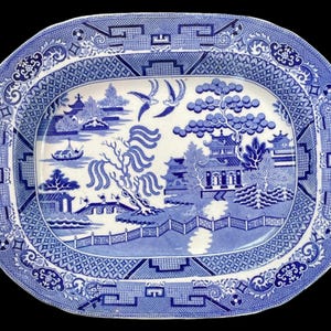 Könnte beinhalten: Eine ovale Servierplatte in Blau und Weiß mit einem traditionellen Weidenmuster. Das Muster zeigt eine Brücke, eine Pagode, einen Weidenbaum und Vögel.