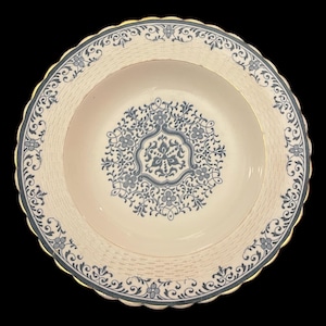 May include: A white ceramic soup bowl with a blue and white floral design. The bowl has a scalloped edge and a gold rim.