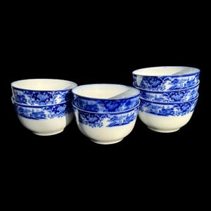 May include: A collection of white and blue porcelain bowls. The bowls have a blue floral and landscape design around the rim and base. The bowls are stacked in groups of two and three, with a total of seven bowls visible.