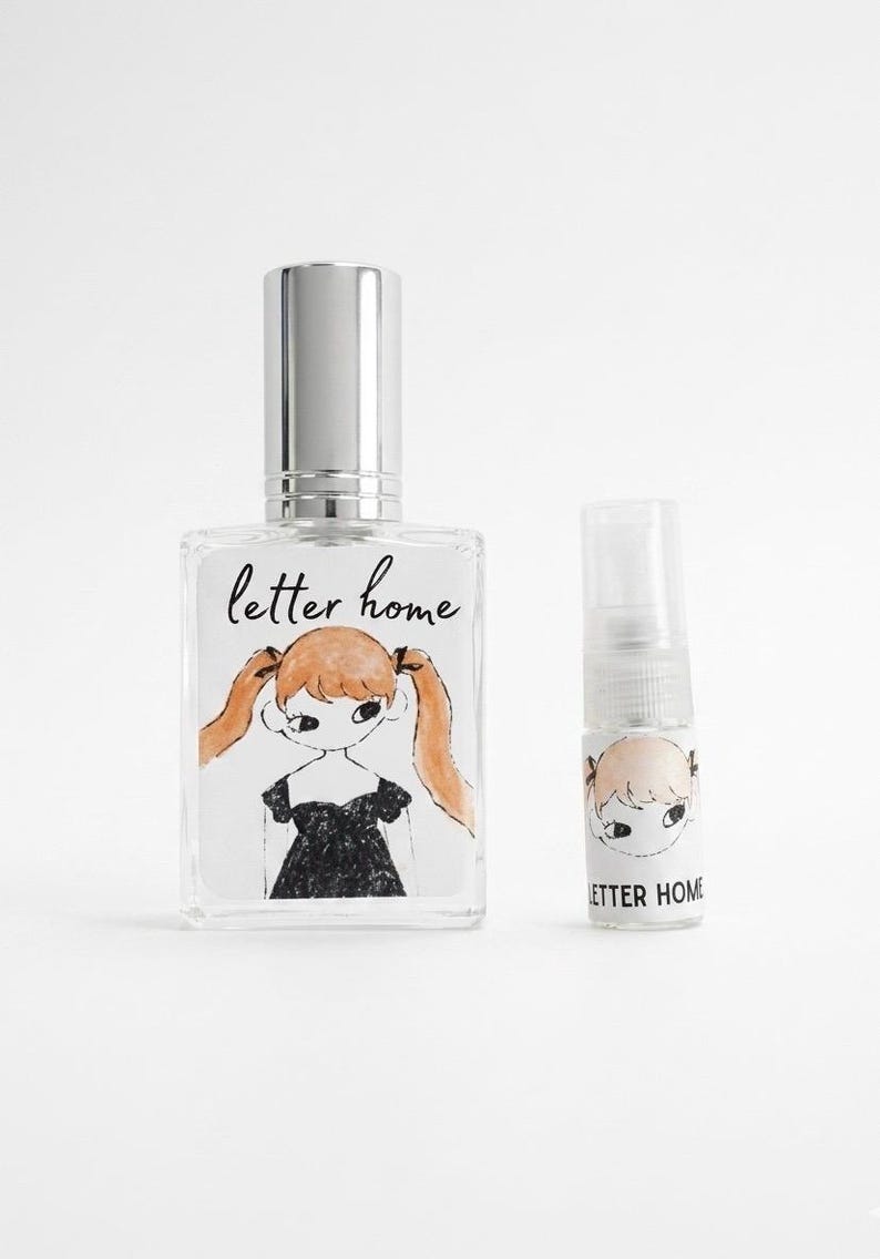 Pu&ograve; includere: Un flacone di profumo rettangolare in vetro con tappo argentato e un flacone spray cilindrico pi&ugrave; piccolo. Entrambi presentano un'etichetta con il testo "letter home" e l'illustrazione di una persona con codini arancioni e abito nero.