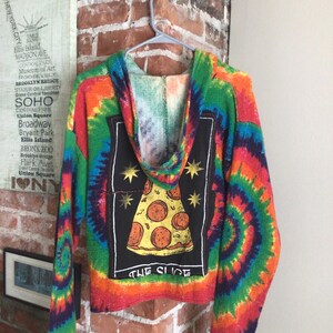 May include: A long-sleeve hoodie featuring a vibrant multi-colored tie-dye pattern. The back displays a large rectangular black patch with a graphic of a pepperoni pizza slice, four gold stars, and the text "THE SLICE" printed in white.