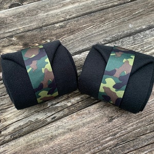 Könnte beinhalten: Zwei schwarze Handgelenkbandagen mit Camouflage-Muster. Die Bandagen bestehen aus einem weichen Material und sind für die Unterstützung beim Gewichtheben oder anderen Übungen konzipiert. Das Camouflage-Muster umfasst Grün-, Braun- und Beigetöne.