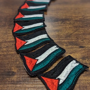 May include: A row of embroidered patches featuring the Palestinian flag. The patches are black with a red triangle, a white stripe, and a green stripe.