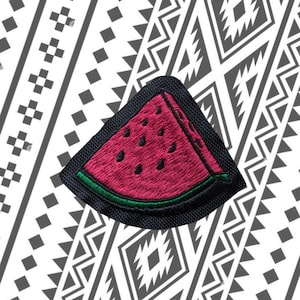 May include: A black felt patch with a red and green embroidered watermelon slice. The watermelon slice has black seeds.