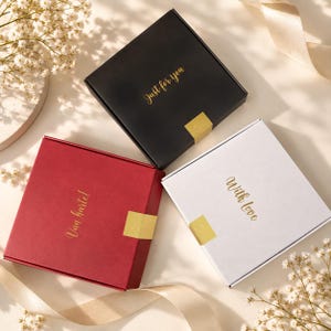 Op de afbeelding: Drie vierkante geschenkdozen in zwart, rood en wit. De zwarte doos heeft de gouden tekst Just for you, de rode doos de gouden tekst Van hartel en de witte doos de gouden tekst With love. Elke doos is voorzien van een gouden zegel.