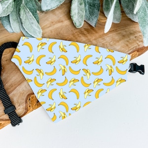 Può includere: Un bandana per cani blu chiaro con un motivo di banane gialle. Il bandana ha una cinghia regolabile nera con una fibbia di plastica.