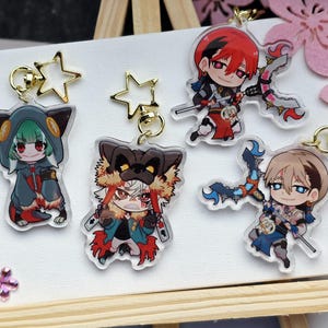 Könnte beinhalten: Sammlung von Schlüsselanhängern mit Anime-Charakteren. Jeder Schlüsselanhänger zeigt ein einzigartiges Charakterdesign mit leuchtenden Farben und detaillierten Kunstwerken. Schlüsselanhänger sind an goldenen sternförmigen Verschlüssen befestigt.