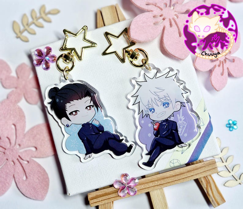 May include: Two anime-style acrylic keychains featuring characters in dark blue suits. One has black hair, the other white. Both are attached to gold star-shaped clasps. The background includes pink flower cutouts and the word "Chuuya".