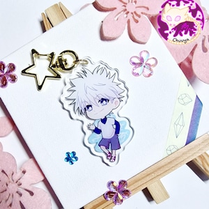Op de afbeelding: Een sleutelhanger met een wit en blauw anime-personage met een gouden sterbedel. Het personage heeft wit haar en draagt een wit shirt en een blauwe broek. De sleutelhanger is op een witte achtergrond met roze bloemen.