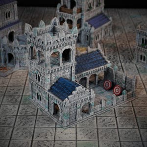 Könnte beinhalten: Ein graues Steingebäude mit einem Turm und einem blauen Dach. Das Gebäude hat einen kleinen Innenhof mit zwei roten und weißen Zielen. Das Gebäude ist aus einem strukturierten Material gefertigt und wirkt realistisch.