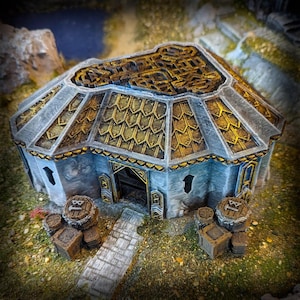 May include: A miniature model of a round building with a grey and gold roof. The building has a small door and windows. The building is surrounded by a grassy area with several barrels.