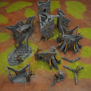 Könnte beinhalten: Eine Sammlung grauer Miniatur-Burgruinen mit goldenen Akzenten und Holzelementen. Die Teile sind auf einer braunen und grünen Oberfläche angeordnet, was auf ein Tabletop-Spiel hindeutet. Die Strukturen variieren in Größe und Form, mit zerbrochenen Mauern und Türmen.