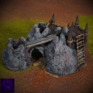 Puede incluir: Una pieza de terreno de fantasía en miniatura que presenta una estructura rocosa con un puente, un techo de madera y una escalera. Las rocas son grises con acentos rojizos, y el techo es marrón. La escena está ambientada sobre una superficie marrón y verde.