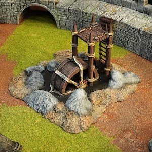 Könnte beinhalten: Miniatur-Diorama eines Wasserrads und einer Brücke. Das Wasserrad ist braun und teilweise in einem kleinen Becken versunken, das von Felsen umgeben ist. Eine Holzbrücke mit einer Leiter steht über dem Rad. Die Szene spielt auf einem grasbewachsenen und felsigen Gelände.