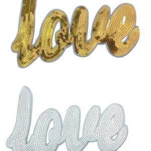 May include: Two iron-on patches with the word "love" in a cursive font. The top patch is gold and the bottom patch is white.
