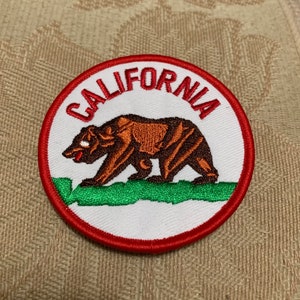 May include: A red, white, and green embroidered patch with the word "CALIFORNIA" in red lettering and a brown bear walking on a green field.