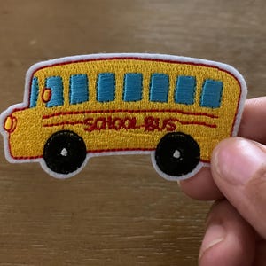 May include: Yellow embroidered iron-on patch of a school bus with the words "School Bus" in red.