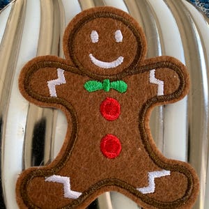 May include: A brown gingerbread man applique with white icing details, a green bow tie, and two red buttons.