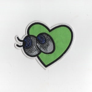 May include: Green heart-shaped patch with two black and white eyes with blue pupils.