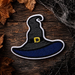 May include: An embroidered patch shaped like a pointed hat with a dark gray crown, a navy blue brim, and a white border. The hat features a black band around the base with a yellow buckle detail in the center, all rendered in detailed stitching.
