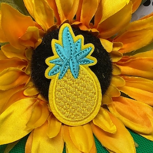 May include: An embroidered pineapple patch featuring a bright yellow fruit body with a textured stitch pattern and a vibrant turquoise green leafy top. The patch is oval-shaped with a yellow border, showcasing detailed needlework and thread density.