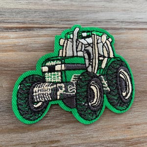 May include: Green and black embroidered tractor patch with white details. The tractor has large wheels and a cab with a roll cage.