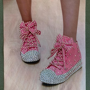 May include: Pink high-top sneakers with a large bow on the front and covered in silver rhinestones.