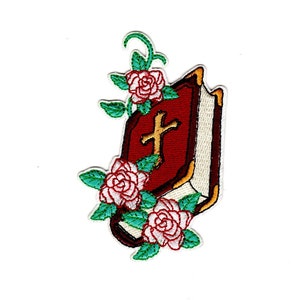 May include: Embroidered iron-on patch featuring a red book with a gold cross and a gold border. The book is surrounded by green vines and pink roses.