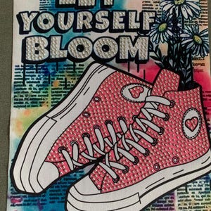 May include: Pink high-top sneakers with white laces and a heart design on the side. The sneakers are covered in rhinestones and are set against a background of a newspaper print with the words "Let Yourself Bloom" in white rhinestones.