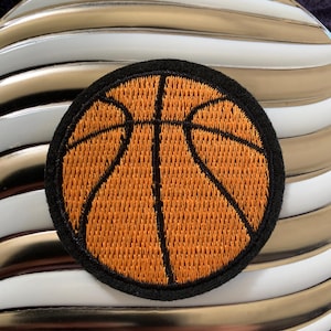 May include: Round orange basketball patch with black stitching and a black border. The patch is on a white and gold striped background. The basketball design features black lines to represent the ball's panels.