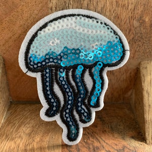 May include: A blue and white sequined jellyfish patch with black outlines. The patch is made of felt and sequins.