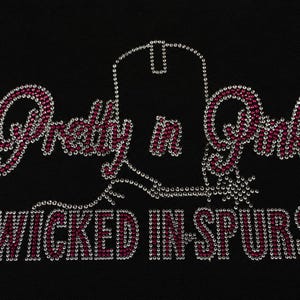May include: A rhinestone transfer design on a black background featuring the text Pretty n Pink in pink and clear crystals. A central outline of a cowboy boot with a spur is also formed by clear crystals, with the text WICKED IN SPURS below.