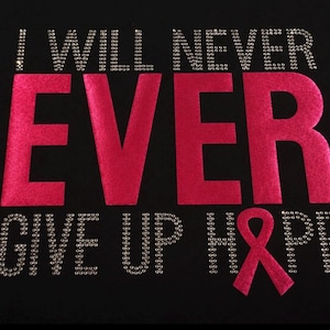 May include: A black fabric surface featuring the text I WILL NEVER EVER GIVE UP HOPE. The words I WILL NEVER and GIVE UP HOPE are rendered in small silver rhinestones, while the word EVER is in large, bold, hot pink velvet-textured letters.