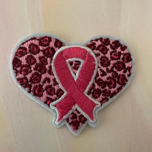 May include: Pink ribbon in the shape of a heart with a leopard print background. The ribbon is a symbol of breast cancer awareness.