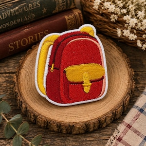 May include: An embroidered patch shaped like a backpack with a red main compartment, a yellow front pocket, yellow side panels, and a white border. The design features a small yellow top handle and a yellow strap detail on the front pocket.